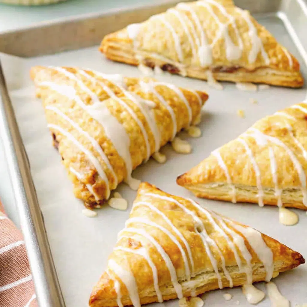 Easy Puff Pastry Apple Turnovers 9 Golden brown puff pastry apple turnovers arranged on a white plate with one broken open to show the tender cinnamon-spiced apple filling inside