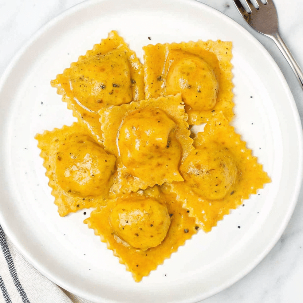 Butternut squash ravioli on a white plate with brown butter sauce and sage leaves