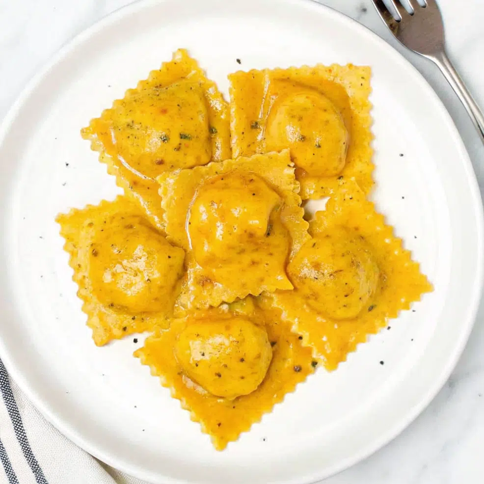 Homemade Butternut Squash Ravioli 6 Butternut squash ravioli on a white plate with brown butter sauce and sage leaves