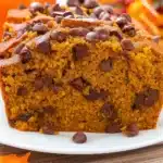Best Chocolate Chip Pumpkin Bread 8 Golden brown chocolate chip pumpkin bread sliced on a wooden cutting board, showing moist interior with chocolate chips throughout, surrounded by autumn pumpkins and spices