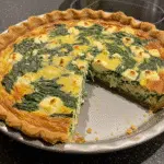 Golden-brown crustless spinach onion and feta quiche in a white ceramic pie dish, garnished with fresh dill and cut into wedges
