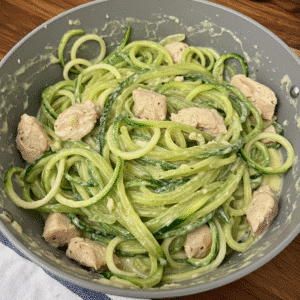 Creamy zucchini noodle chicken alfredo in a white bowl with fresh parsley garnish and grated Parmesan cheese on top