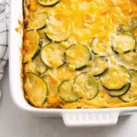 Easy Keto Zucchini Casserole 10 Golden brown keto zucchini casserole in a white baking dish, topped with melted Colby-Jack cheese and showing layers of tender zucchini in a creamy sauce