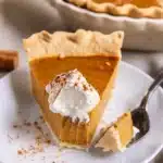 Best Pumpkin Pie Recipe 8 Golden brown pumpkin pie with flaky crust, garnished with sugared cranberries and whipped cream, served on a rustic wooden table with fall decorations