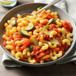 A colorful bowl of Tomato Zucchini Pasta with golden zucchini rounds, burst cherry tomatoes, and fresh basil, topped with grated Parmesan cheese