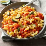 Healthy Tomato Zucchini Pasta 10 A colorful bowl of Tomato Zucchini Pasta with golden zucchini rounds, burst cherry tomatoes, and fresh basil, topped with grated Parmesan cheese
