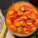 Spicy Pickled Carrots 5 Colorful spicy pickled carrots with red onion and jalapeños in a glass jar, showing the diagonal-cut carrots covered in seasoned brine