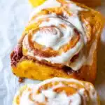 Best Pumpkin Cinnamon Rolls 10 Freshly baked pumpkin cinnamon rolls with maple cream cheese icing in a baking pan, golden brown and perfectly swirled