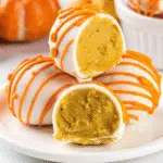 No Bake Pumpkin Cheesecake Balls 5 Bite-sized orange No Bake pumpkin cheesecake balls coated in smooth white chocolate with decorative orange drizzle, arranged on a white serving platter with fall leaves in the background