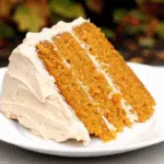 Homemade Pumpkin Spice Cake 5 A slice of moist pumpkin spice cake on a white plate with a fork, showing the tender orange-colored crumb studded with raisins.
