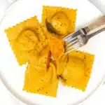 Butternut squash ravioli on a white plate with brown butter sauce and sage leaves