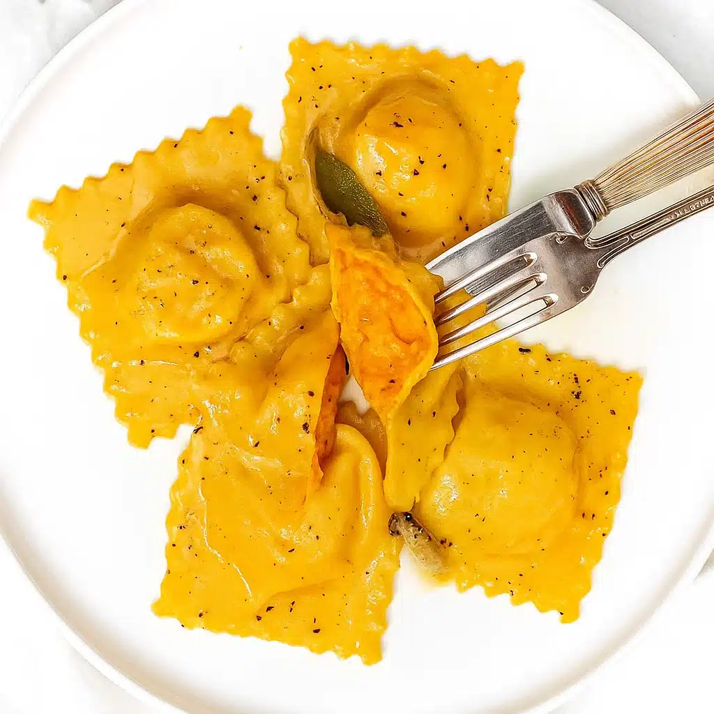 Butternut squash ravioli on a white plate with brown butter sauce and sage leaves