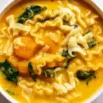 A steaming bowl of Butternut Squash Lasagna Soup with Kale and Mozzarella cheese and fresh kale, served with crusty bread on a wooden table.