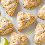 Apple Cinnamon Scones 10 Eight golden apple cinnamon scones with white glaze drizzled on top sitting on wooden cutting board with fresh apple slices and cinnamon sticks