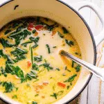 Crack Chicken Soup 8 A creamy, loaded crack chicken soup in a white bowl topped with melted cheddar cheese, crispy bacon bits, and green onions, with a wooden spoon beside it