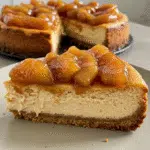 Caramel Apple Pie Cheesecake 8 A slice of caramel apple pie cheesecake on a white plate, showing layers of graham cracker crust, creamy cheesecake filling studded with cinnamon apples, topped with golden streusel and drizzled with salted caramel sauce.