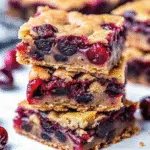 Chocolate Chip Cherry Bars 8 Golden brown chocolate chip cherry bars cut into squares in a parchment-lined baking pan, showing melted chocolate chips and bright red cherry pieces throughout the chewy texture