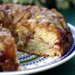Irresistible Apple Fritter Cake 10 A slice of layered apple fritter cake on a white plate, showing moist yellow cake layers with chunks of cinnamon apples and brown sugar swirls, topped with white glaze dripping down the sides.