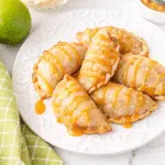 Golden brown caramel apple empanadas on a white plate with melted caramel drizzle, showcasing flaky pastry and gooey caramel filling