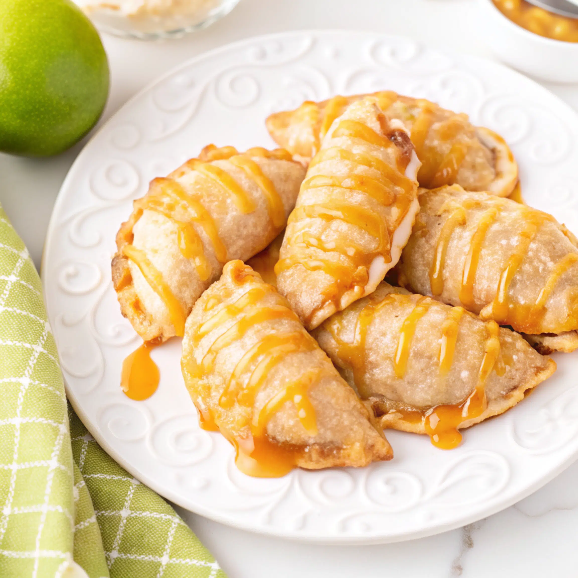 Golden brown caramel apple empanadas on a white plate with melted caramel drizzle, showcasing flaky pastry and gooey caramel filling