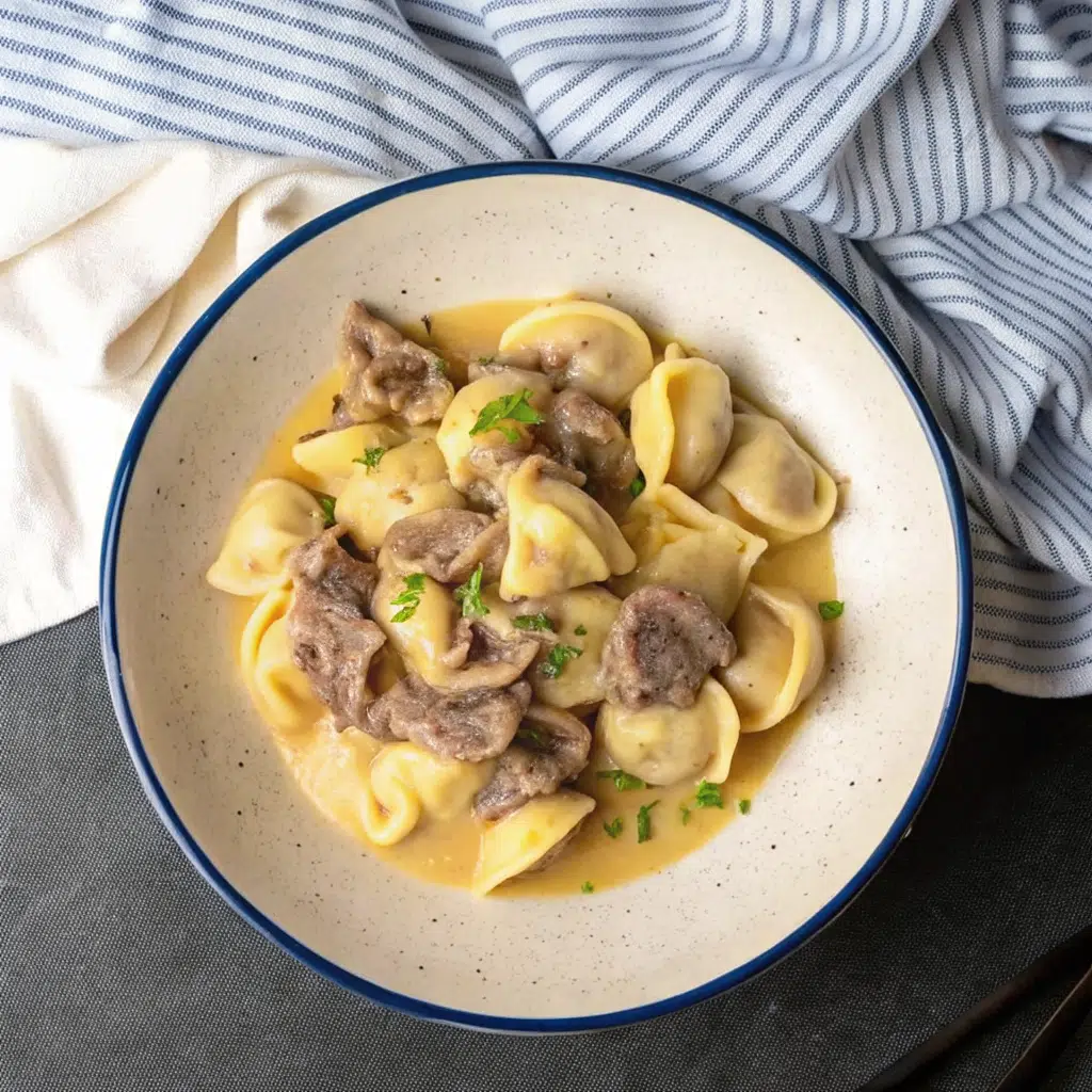 A creamy plate of Cheesesteak Tortellini in Provolone Saucemixed with tender sliced beef, colorful bell peppers and onions, all coated in a rich golden provolone cheese sauce