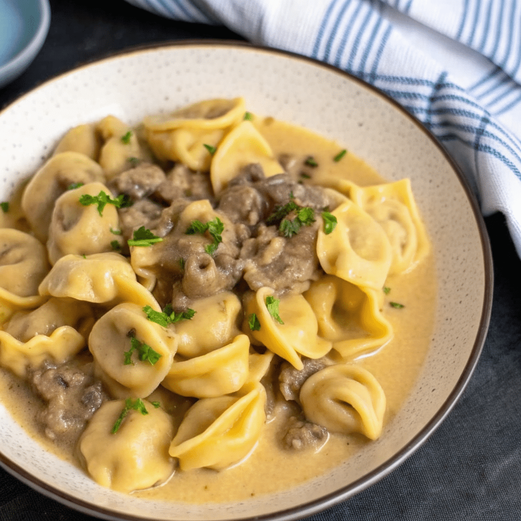 A creamy plate of Cheesesteak Tortellini in Provolone Saucemixed with tender sliced beef, colorful bell peppers and onions, all coated in a rich golden provolone cheese sauce