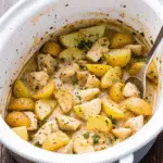 Golden garlic parmesan chicken and potatoes in a white crockpot, topped with melted mozzarella cheese and fresh herbs