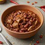 Best Beef Chili Recipe 5 A steaming bowl of hearty beef chili topped with sour cream, cheddar cheese, and fresh cilantro, served with cornbread on a rustic wooden table.