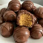 Golden-brown Butterfinger balls coated in smooth chocolate, garnished with crushed Butterfinger pieces, arranged on a white serving platter