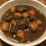 Old Fashioned Beef Stew 5 A steaming bowl of rich beef stew with tender chunks of beef, colorful vegetables, and thick savory broth, garnished with fresh parsley