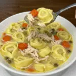 Bowl of chicken tortellini soup with vegetables and shredded chicken in clear broth, garnished with fresh parsley