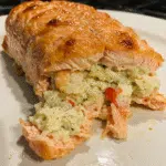 Golden crab shrimp stuffed salmon fillets on white plate garnished with fresh parsley and lemon wedges