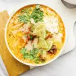 Slow Cooker Mexican Street Corn Soup 5 A bowl of creamy Mexican street corn soup topped with crispy bacon, cotija cheese, cilantro and lime wedges, photographed from above on a rustic wooden table