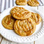 Soft, golden-brown salted caramel cookies drizzled with caramel sauce and topped with flaky sea salt on parchment paper