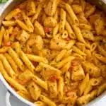 Creamy Cajun chicken pasta in a large skillet with tender penne noodles, seasoned chicken pieces, diced tomatoes, and sliced green onions garnish