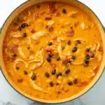 A bowl of creamy chicken enchilada soup topped with shredded cheese, sour cream, and fresh cilantro, served with tortilla chips on a rustic wooden table.