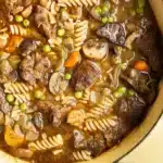 Beef Stew and Noodles 5 A steaming bowl of homemade beef stew and noodles with tender beef chunks, vegetables, and egg noodles in a rich brown broth, garnished with fresh parsley