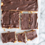 Layers of Christmas Crack candy showing golden caramel over saltine crackers topped with smooth dark chocolate, broken into irregular pieces on parchment paper.
