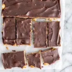 Layers of Christmas Crack candy showing golden caramel over saltine crackers topped with smooth dark chocolate, broken into irregular pieces on parchment paper.