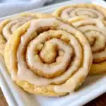 Soft cinnamon roll cookies with visible cinnamon swirls, drizzled with white vanilla icing, arranged on parchment paper