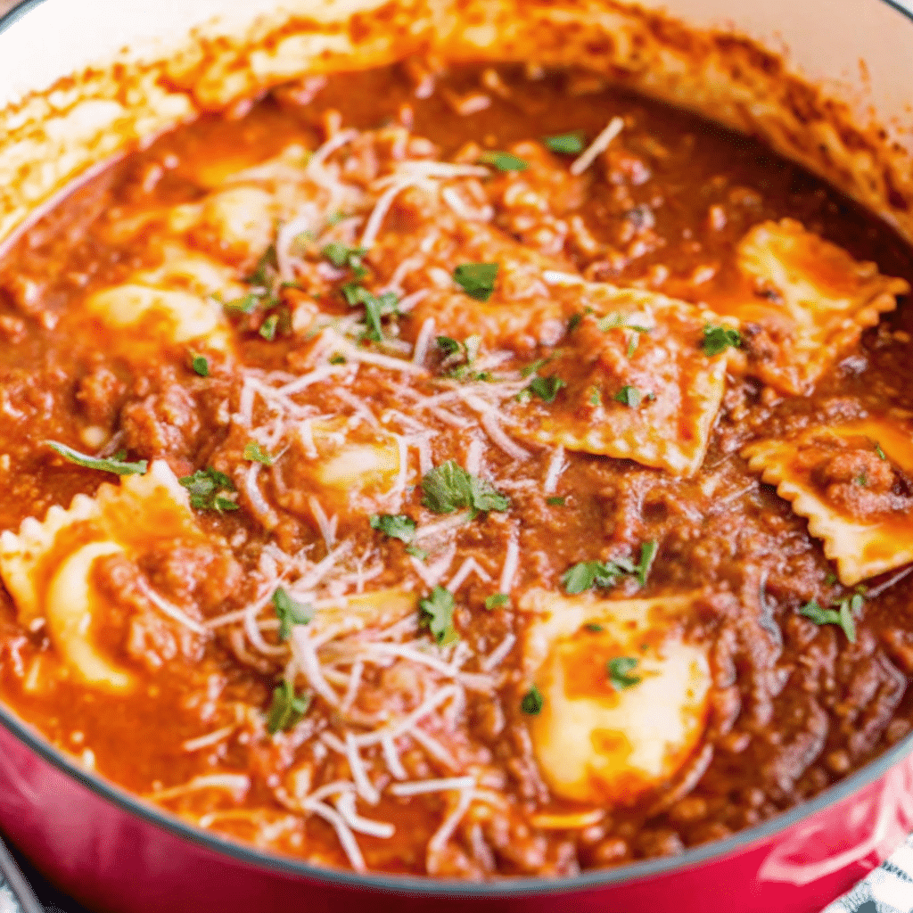 A steaming bowl of ravioli soup with cheese ravioli floating in rich tomato broth, garnished with fresh parsley and grated Parmesan cheese
