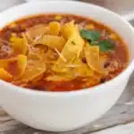 Taco Soup Recipe 5 Steaming bowl of hearty taco soup topped with shredded cheese, diced avocado, and tortilla strips on rustic wooden table