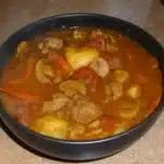 French Beef Stew 5 A hearty bowl of French beef stew with tender chunks of beef, carrots, and potatoes in a rich tomato-based broth, garnished with fresh herbs