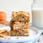 Square apple brownies golden edges visible tender apple chunks throughout topped cinnamon-sugar crystals cut neat squares arranged white ceramic plate rustic wooden background