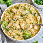 A skillet filled with creamy cheesy chicken broccoli orzo with tender chicken pieces, bright green broccoli florets, and melted cheese sauce, garnished with fresh herbs and Parmesan