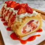 Strawberry shortcake sushi rolls sliced into perfect rounds showing swirls of vanilla sponge cake white whipped cream and fresh red strawberries arranged on white plate