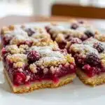 Golden buttery cranberry bars with crumble topping and fresh cranberries showing through, cut into squares on parchment paper