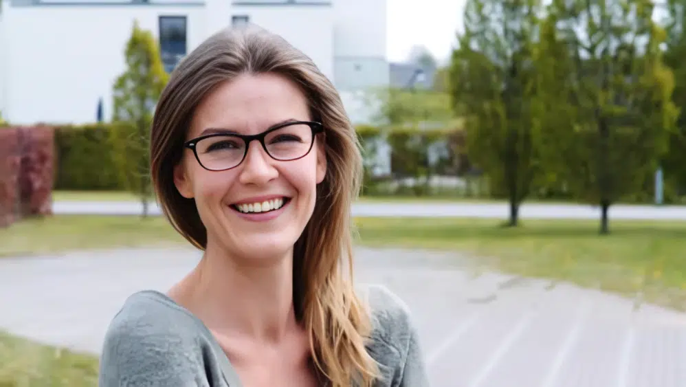 Smiling woman with glasses standing outdoors on a bright day