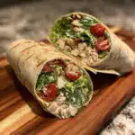 Chicken Caesar wrap cut in half showing layers of chopped romaine lettuce, grilled chicken, cherry tomatoes, parmesan cheese, and croutons wrapped in a flour tortilla with creamy Caesar dressing