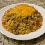 Casserole dish with hamburger rice topped with melted golden mozzarella cheese showing ground beef and rice underneath